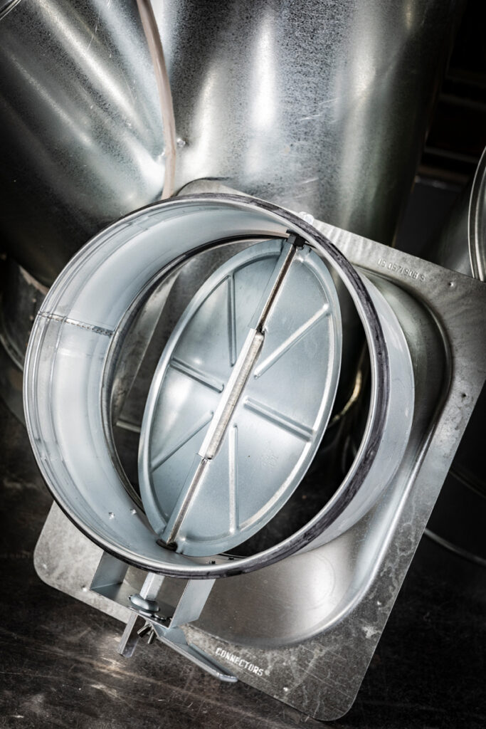 Close-up of a manual volume control damper integrated into a round duct connector, allowing for precise airflow adjustment in custom HVAC duct systems.