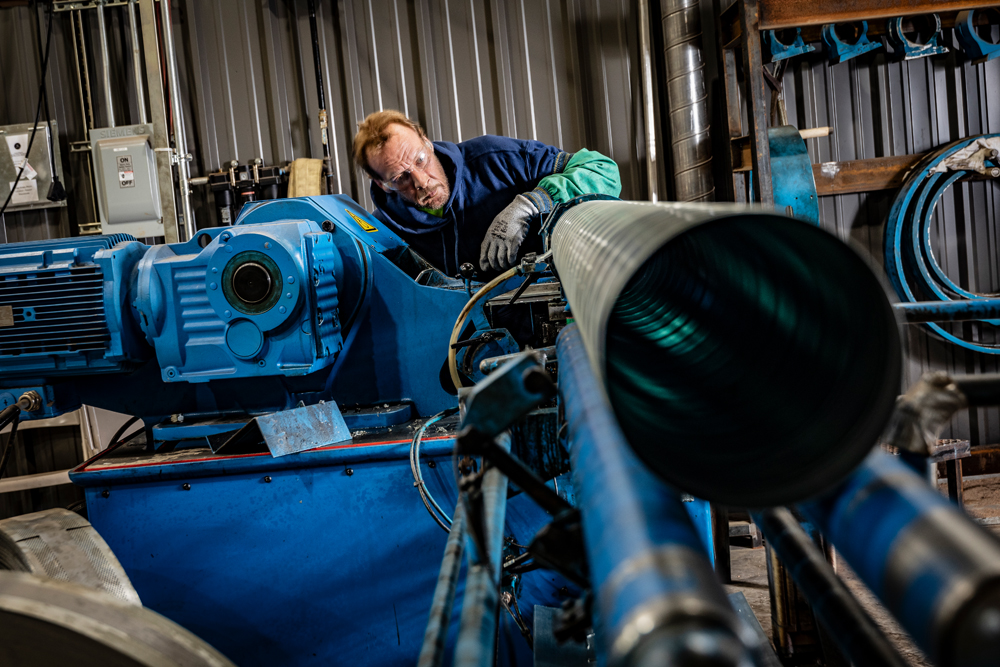 DuctWorx technician operating a spiral duct forming machine, producing high-efficiency round ductwork for commercial and industrial HVAC systems.