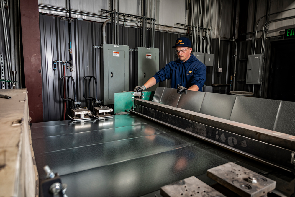 A DuctWorx technician forming a galvanized panel with a sheet metal brake, creating precision bends for rectangular ductwork or custom HVAC fittings.