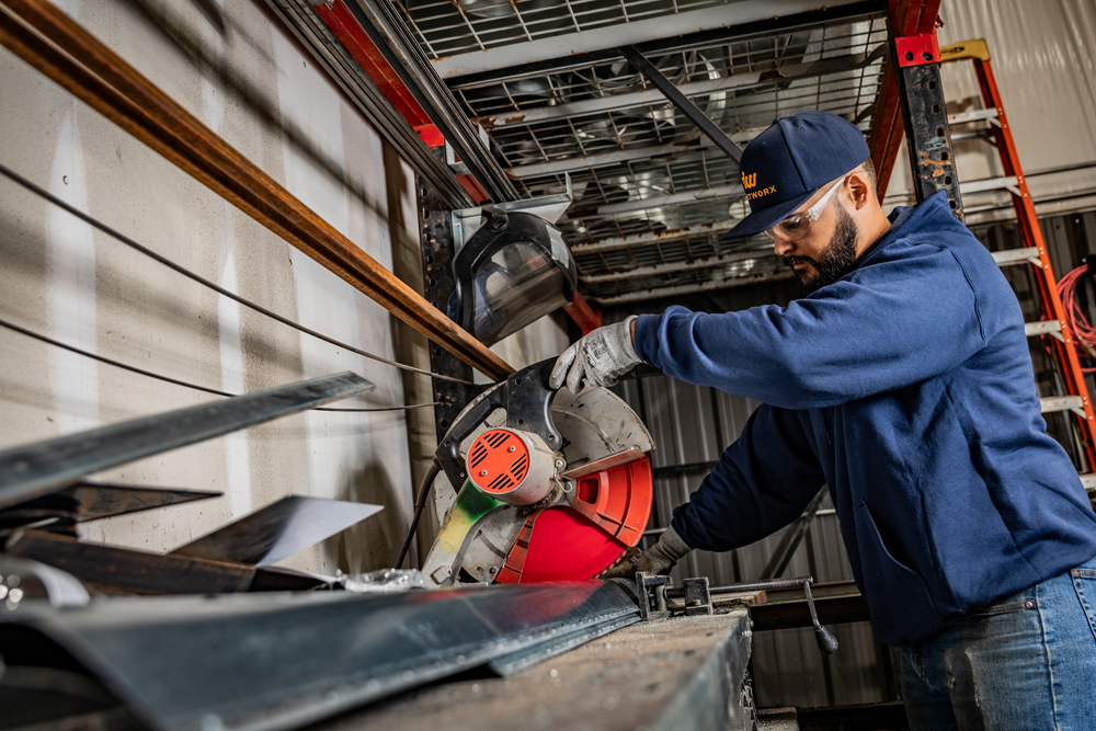 DuctWorx technician cutting steel angle iron for a custom HVAC support bracket, part of the company’s precision-built ductwork infrastructure solutions.