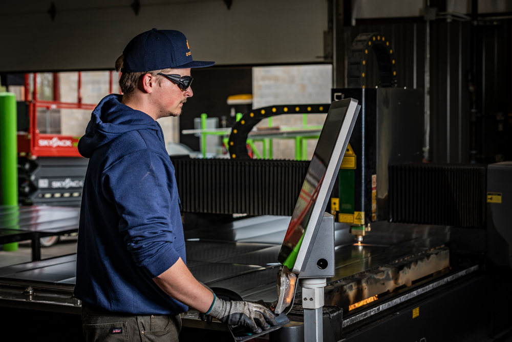 A DuctWorx technician operating a CNC laser cutting machine to fabricate precision sheet metal ductwork components, ensuring accuracy and efficiency in custom HVAC systems.